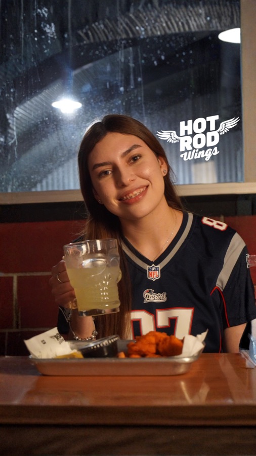 Clienta con jersey de Patriots disfrutando alitas en Hot Rod Wings