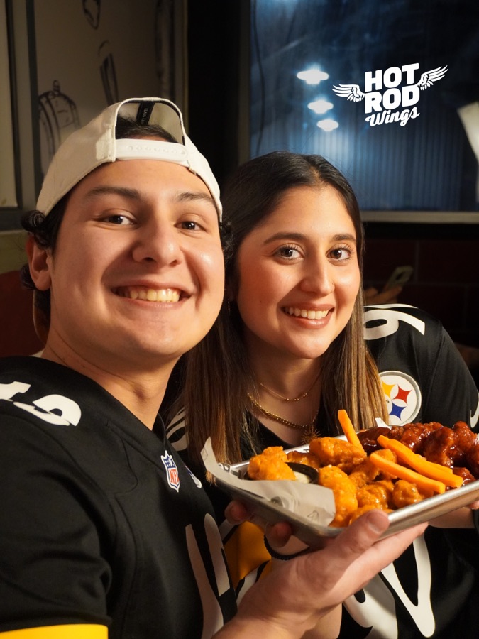 Pareja con jerseys de Steelers con una charola de alitas Hot Rod Wings